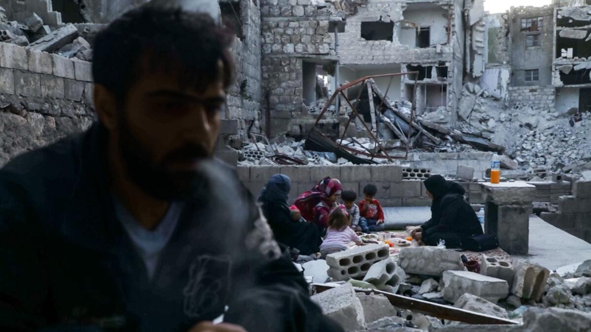 This picture taken on May 4, 2020 during the Muslim holy fasting month of Ramadan shows Tareq Abu Ziad (L), a displaced Syrian from the town of Ariha in the southern countryside of the Idlib province, smoking as members of his family break their fast together for the sunset "iftar" meal, in the midst of the rubble of their destroyed home upon their return to the town for one day after fleeing during the previous military assault by Syrian government forces and their allies. AAREF WATAD / AFP