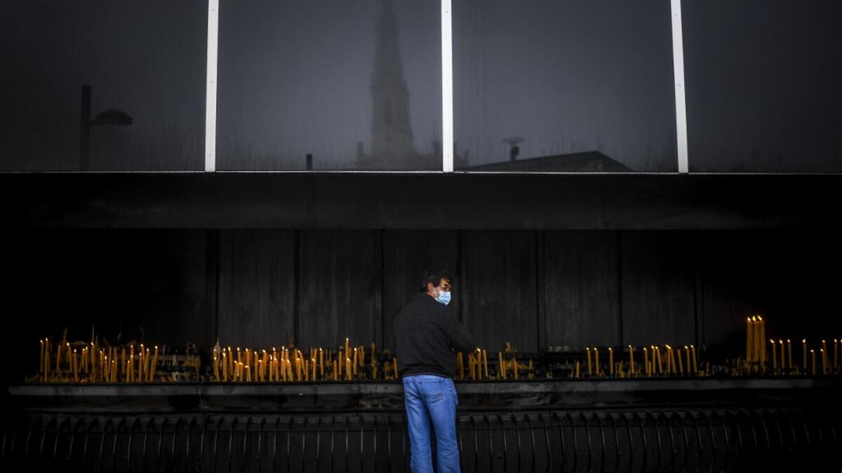 A man wearing a face mask lights a candle during the 103rd anniversary of the apparitions of Our Lady of Fatima at the Fatima shrine in central Portugal on May 13, 2020. Without the crowd of pilgrims it welcomes every year, the shrine of Fatima celebrated the anniversary during a religious ceremony reduced to the bare minimum. PATRICIA DE MELO MOREIRA / AFP