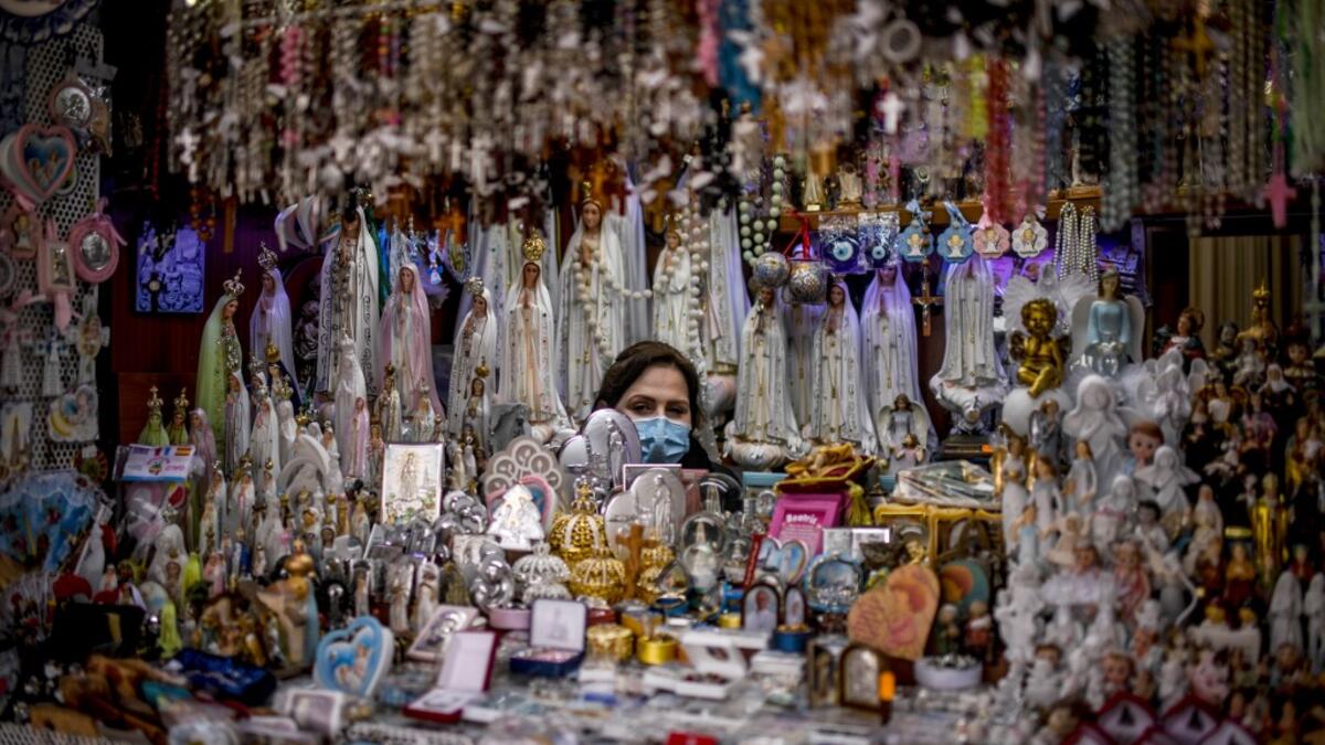 A seller of religious figurines poses at her stall wearing a face mask during the 103rd anniversary of the apparitions of Our Lady of Fatima at the Fatima shrine in central Portugal on May 13, 2020. Without the crowd of pilgrims it welcomes every year, the shrine of Fatima celebrated the anniversary during a religious ceremony reduced to the bare minimum. PATRICIA DE MELO MOREIRA / AFP