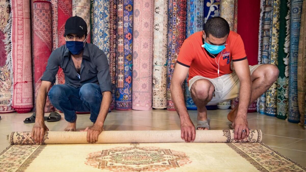 Moroccan rug dealers roll a carpet at a shop in the city of Sale, north of the capital Rabat, on June 3, 2020, during the novel coronavirus pandemic. Artisans in Morocco have been starved of income for almost three months because of the COVID-19 pandemic. The crafts industry represents some seven percent of GDP, with an export turnover last year of nearly 1 billion dirhams ($100 million). FADEL SENNA / AFP