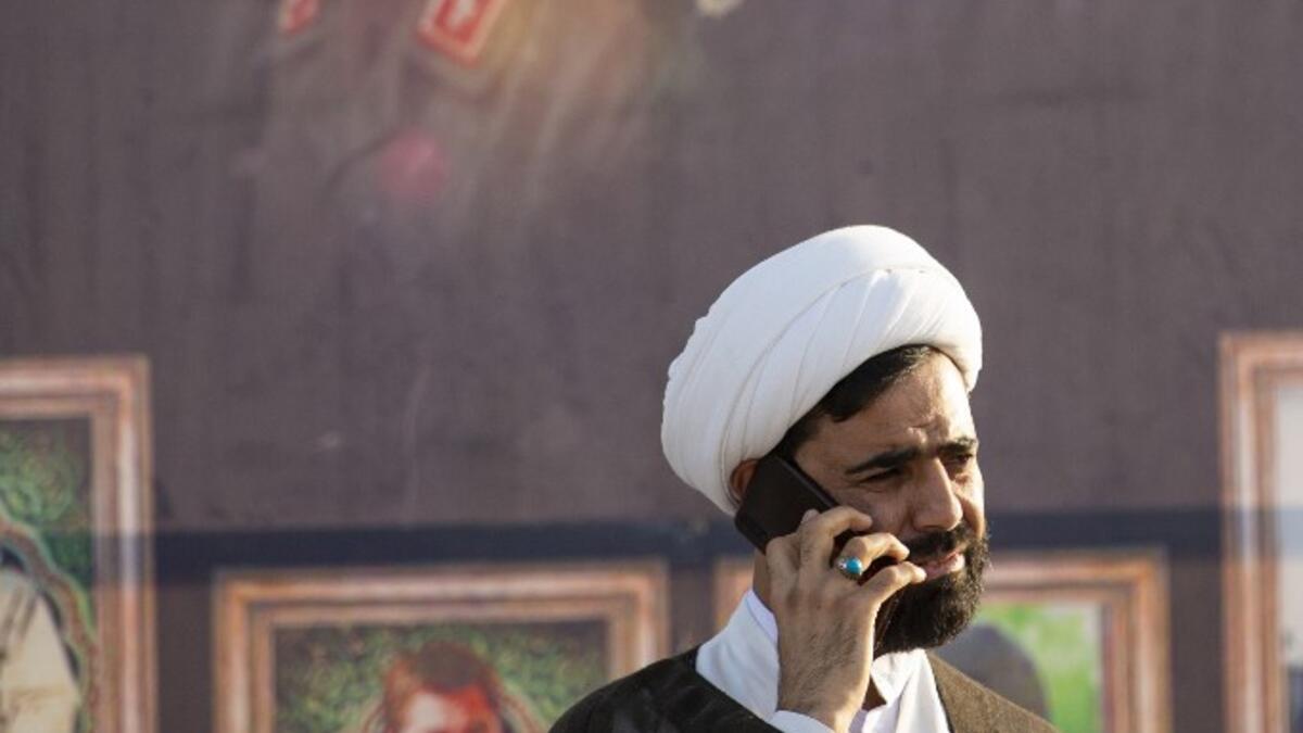 A Muslim cleric speaks on the phone in front of a poster depicting slain Iranian general Qasem Soleimani (L) and slain Iraqi commander Abu Mahdi al-Muhandis during a military parade for Hashed al-Shaabi (Popular Mobilisation) paramilitary force in the southern Iraqi city of Basra on June 14, 2020, marking the sixth anniversary of its founding after Iraq's top Shiite cleric Grand Ayatollah Ali Sistani called to defend the country from the Islamic State group (IS). Hussein FALEH / AFP