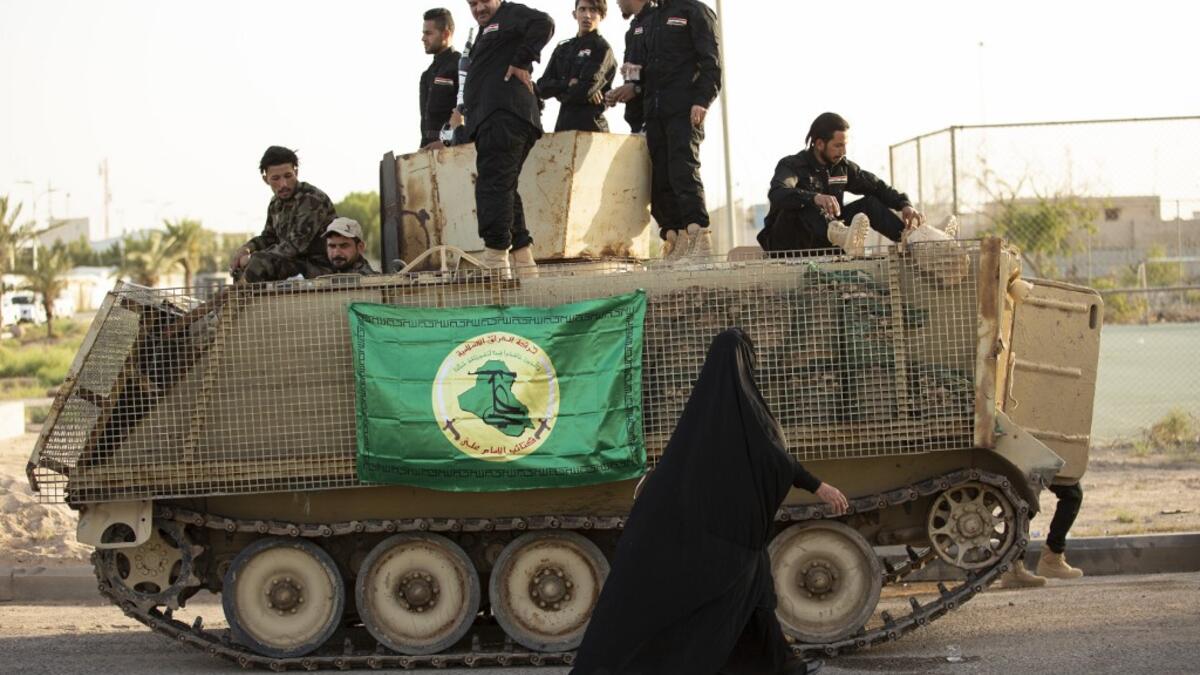 A woman walks past members of the Hashed al-Shaabi (Popular Mobilisation) paramilitary force taking part in a military parade in the southern Iraqi city of Basra on June 14, 2020, marking the sixth anniversary of its founding after Iraq's top Shiite cleric Grand Ayatollah Ali Sistani called to defend the country from the Islamic State group (IS). Hussein FALEH / AFP