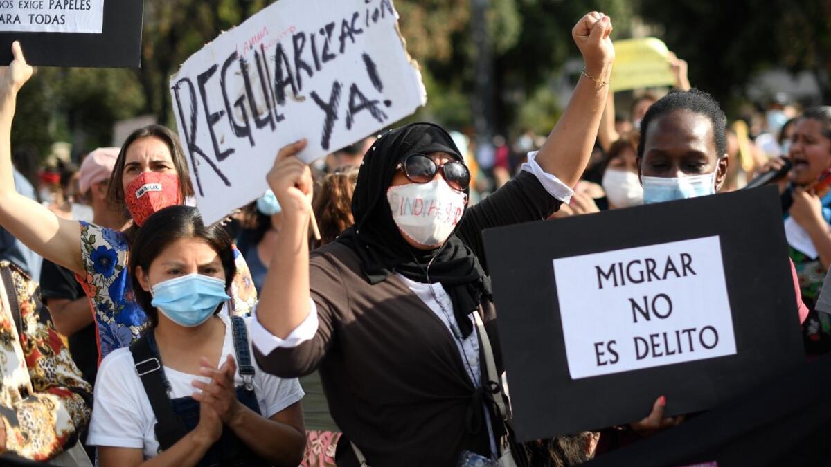 Women hold placrds rading !Legalization now" and "To migrate is not a crime" during a migrant´s demonstration in Barcelona on June 20, 2020, marking World Refugee Day and demanding legal papers for refugees and migrants in Spain. Josep LAGO / AFP