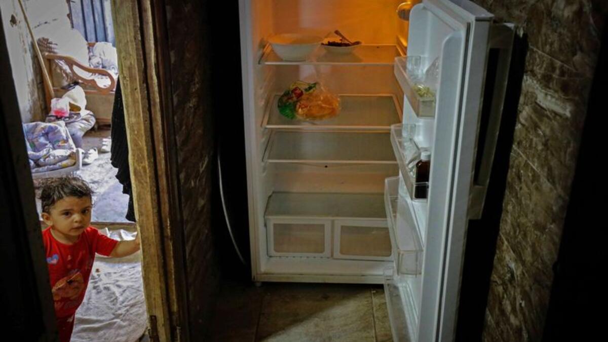 A Lebanese child stands next to an empty refrigerator in their apartment in the port city of Tripoli north of Beirut. Image Credit: AFP