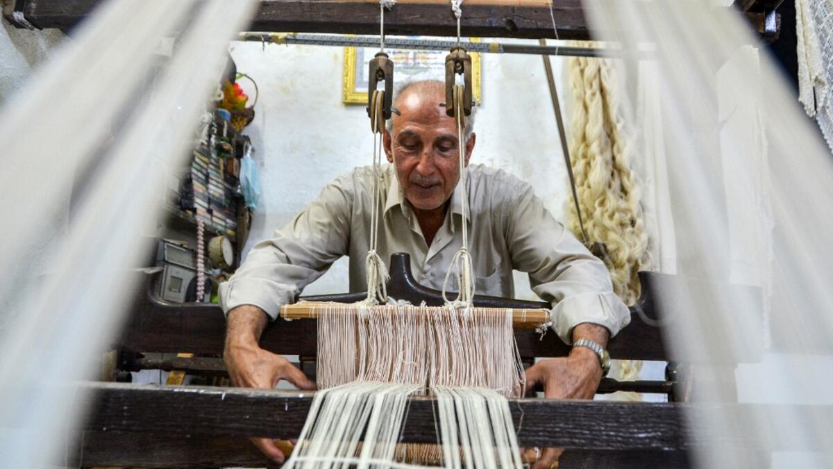 Muhammad Saud, a 65-year-old Syrian silk farmer, handweaves silk threads on a loom at his home workshop in the village of Deir Mama, in west-central Syria on June 22, 2020. MAHER AL MOUNES / AFP