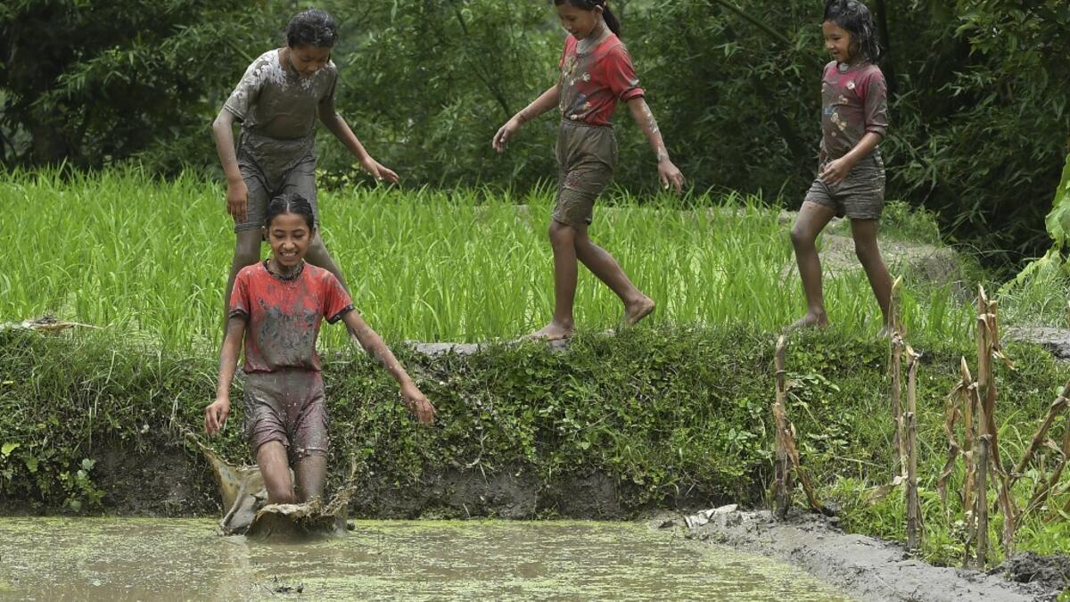 In this photograph taken on June 29, 2020 a mud-covered girls play in a rice paddy field during "National Paddy Day", which marks the start of the annual rice planting season, in Tokha village on the outskirts of Kathmandu. PRAKASH MATHEMA / AFP