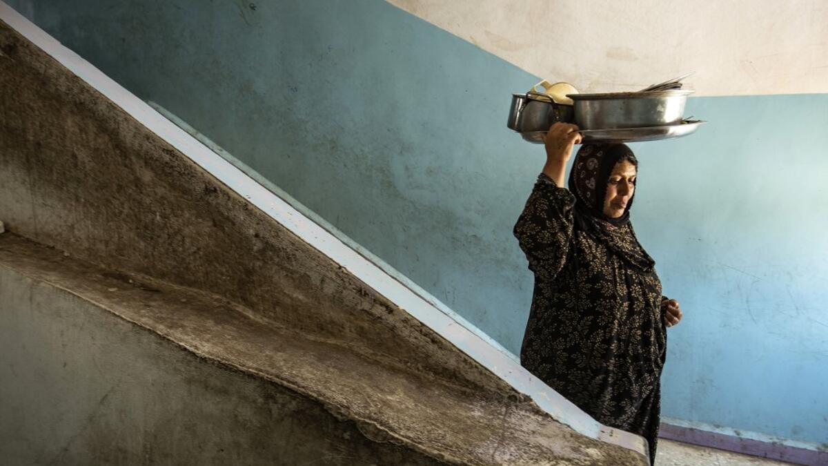 A woman walks down a stairwell while carrying pots on her head at a school building where Syrians -- displaced from the area of Ras al-Ain by the Turkish offensive on the northeast -- are staying in the city of Hasakah, on June 30, 2020. Delil SOULEIMAN / AFP