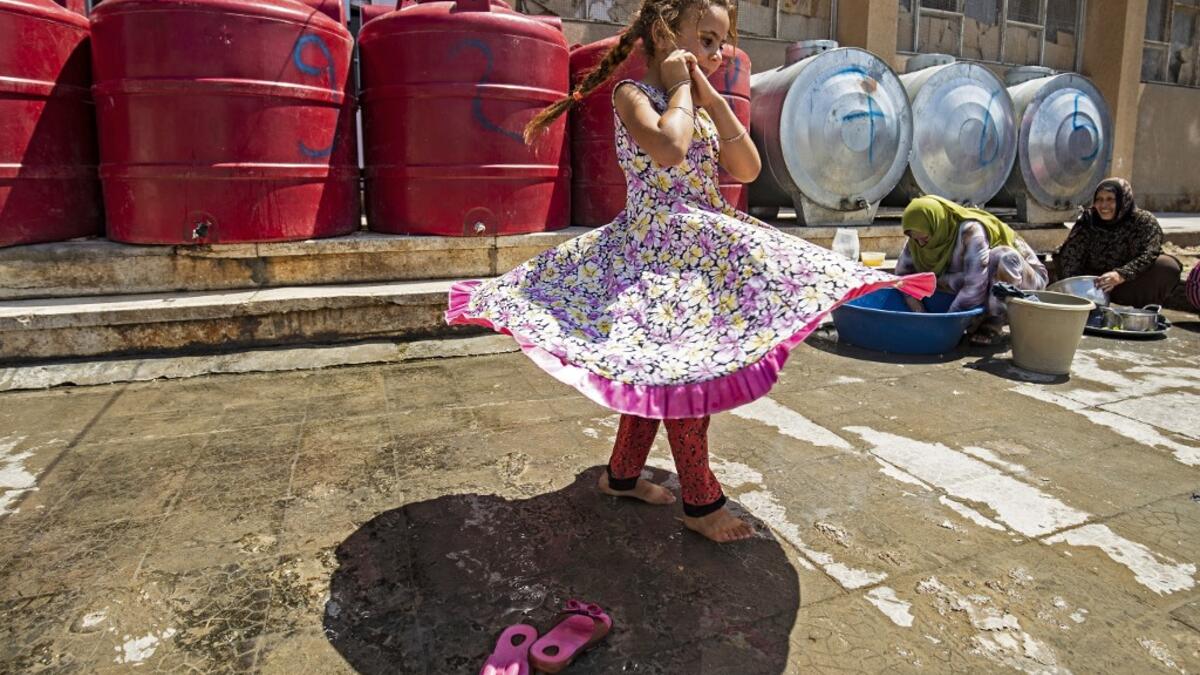 A girl walks past women washing pots and pans by cisterns at the yard of a school building where Syrians -- displaced from the area of Ras al-Ain by the Turkish offensive on the northeast -- are staying in the city of Hasakah, on June 30, 2020. Delil SOULEIMAN / AFP