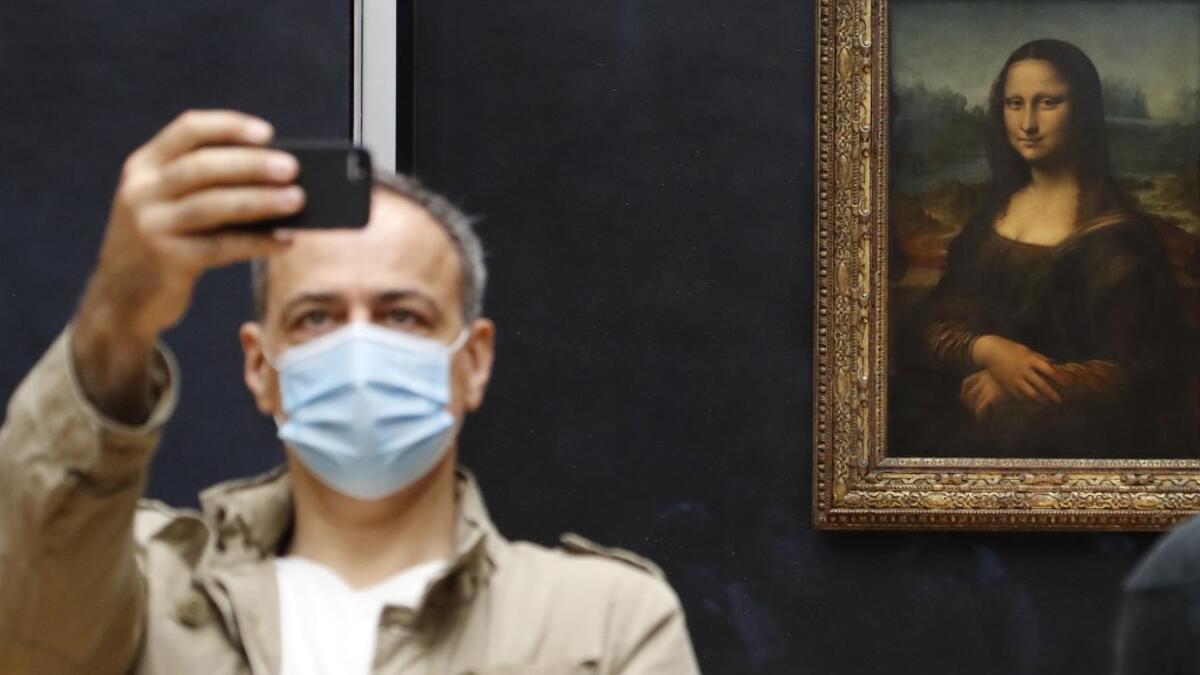 A visitor wearing a protective face mask takes a selfie in front of Leonardo da Vinci's masterpiece "Mona Lisa" also known as "La Gioconda" on the reopening day of the Louvre Museum in Paris on July 6, 2020. FRANCOIS GUILLOT / AFP