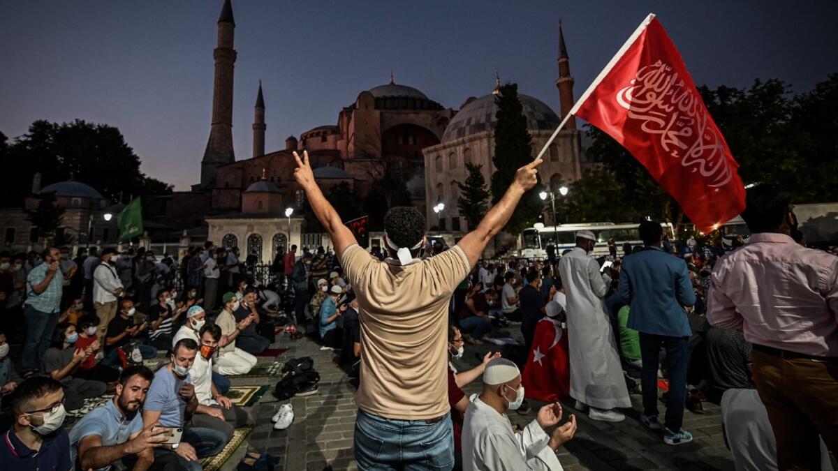 A man flashes the V for Victory hand sign and waves a flag outside the Hagia Sophia museum in Istanbul on July 10, 2020 as people gather to celebrate after a top Turkish court revoked the sixth-century Hagia Sophia's status as a museum, clearing the way for it to be turned back into a mosque. The Council of State, the country's highest administrative court which on July 2 debated a case brought by a Turkish NGO, cancelled a 1934 cabinet decision and ruled the UNESCO World Heritage site would be reopened to