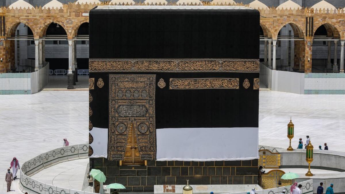 Workers at the Grand Mosque complex in Saudi Arabia's holy city of Mecca, mask-clad due to the COVID-19 coronavirus pandemic, wave and speak to a security guard as they walk around the Kaaba, Islam's holiest shrine, at centre of the complex ahead of the annual Hajj pilgrimage season on July 24, 2020. AFP