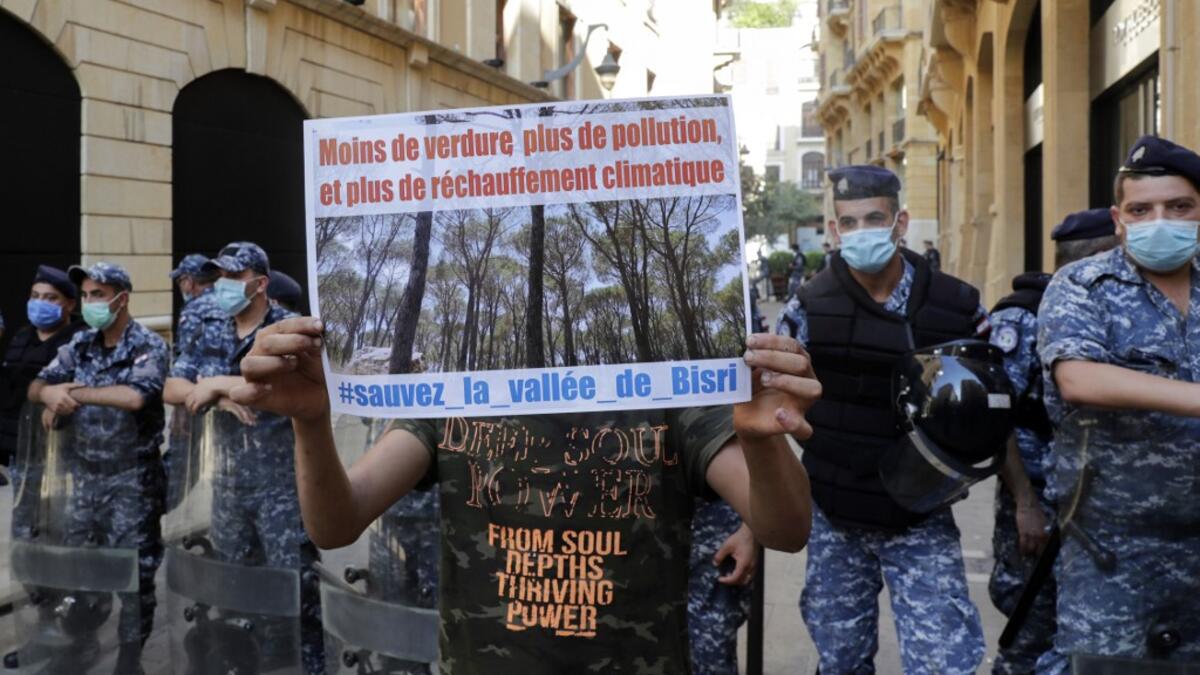 A demonstrator standing in front of members of the Lebanese security forces holds a placard as he takes part in a rally in front of the World Bank offices in the downtown district of the Lebanese capital Beirut on July 25, 2020, to protest against the Bisri dam project, partly financed by the World Bank. The government says the Bisri dam is vital to tackling chronic water shortages. But activists say it will ravage most of the region's farmland and historic sites, and they also fear the consequences of buil