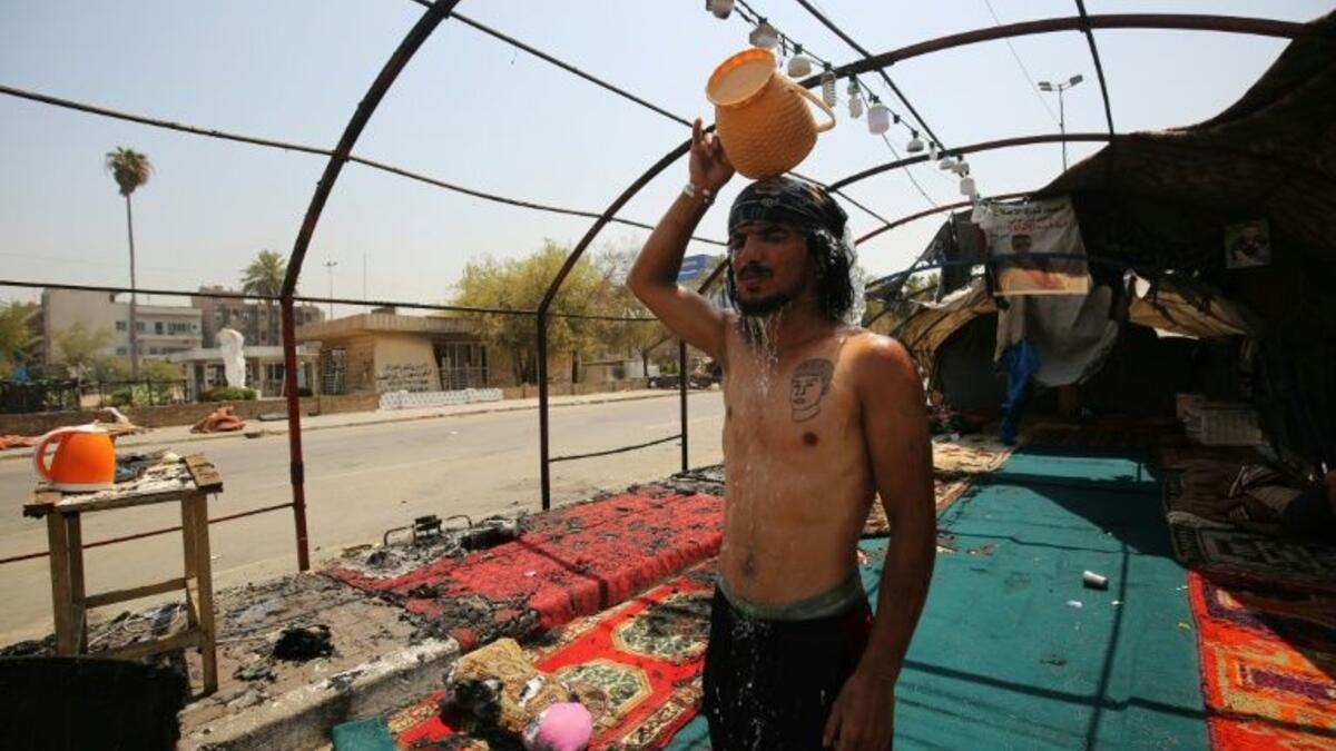 An Iraqi youth pours water over his head to cool down as temperatures soared in Baghdad, standing amid the remains of a protest tent that was burnt the previous night in the capital's Tahrir Square (AFP Photo/AHMAD AL-RUBAYE)