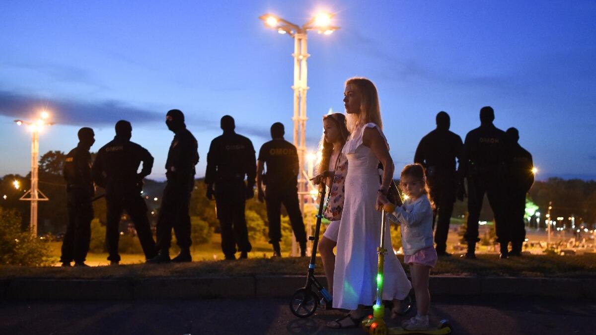 A woman with girls passes riot police officers guarding an area after polls closed in Belarus' presidential election, in Minsk on August 9, 2020. Sergei GAPON / AFP