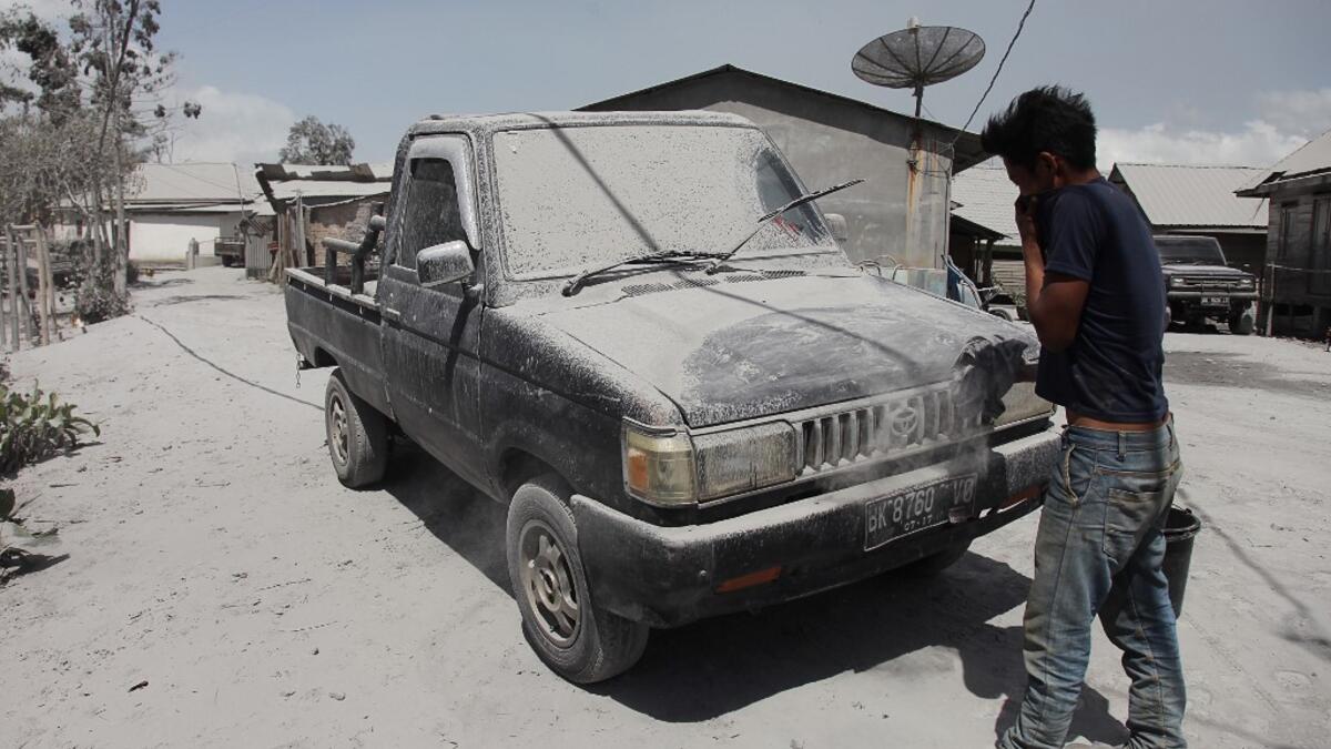 A man cleans a car covered with ash following an eruption by Mount Sinabung at the Sukatepu village in Karo, North Sumatra, on August 10, 2020. Ivan Damanik / AFP