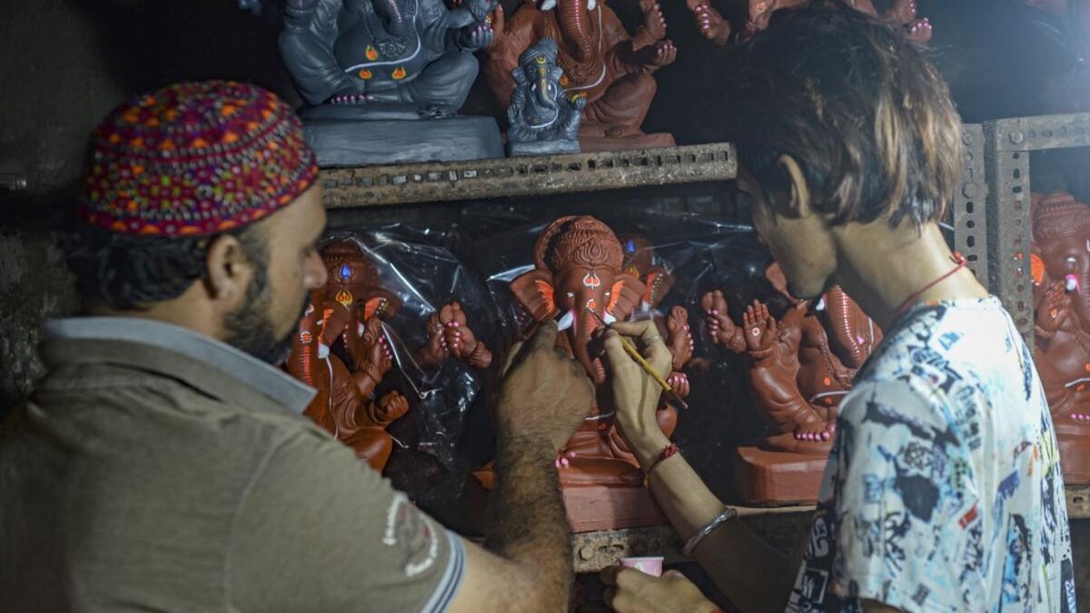 In this picture taken on August 11, 2020, Muslim potter Yusuf Zakaria Galwani (L) instructs an artisan as he gives finishing touches to a clay idol of elephant headed Hindu god Ganesha at his workshop at Kumbharwada inside the Dharavi slums in Mumbai. After the coronavirus pandemic clobbered his pottery business, a Muslim artisan from India's largest slum turned to a Hindu god to revive his fortunes by making environmentally-friendly Ganesha idols for an upcoming festival. In Mumbai's Dharavi slum, Galwani