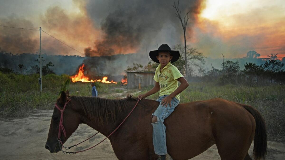 A young boy rides his horse past an illegally lit fire in a section of Amazon rainforest, south of Novo Progresso in Para state, Brazil, on August 15, 2020. CARL DE SOUZA / AFP