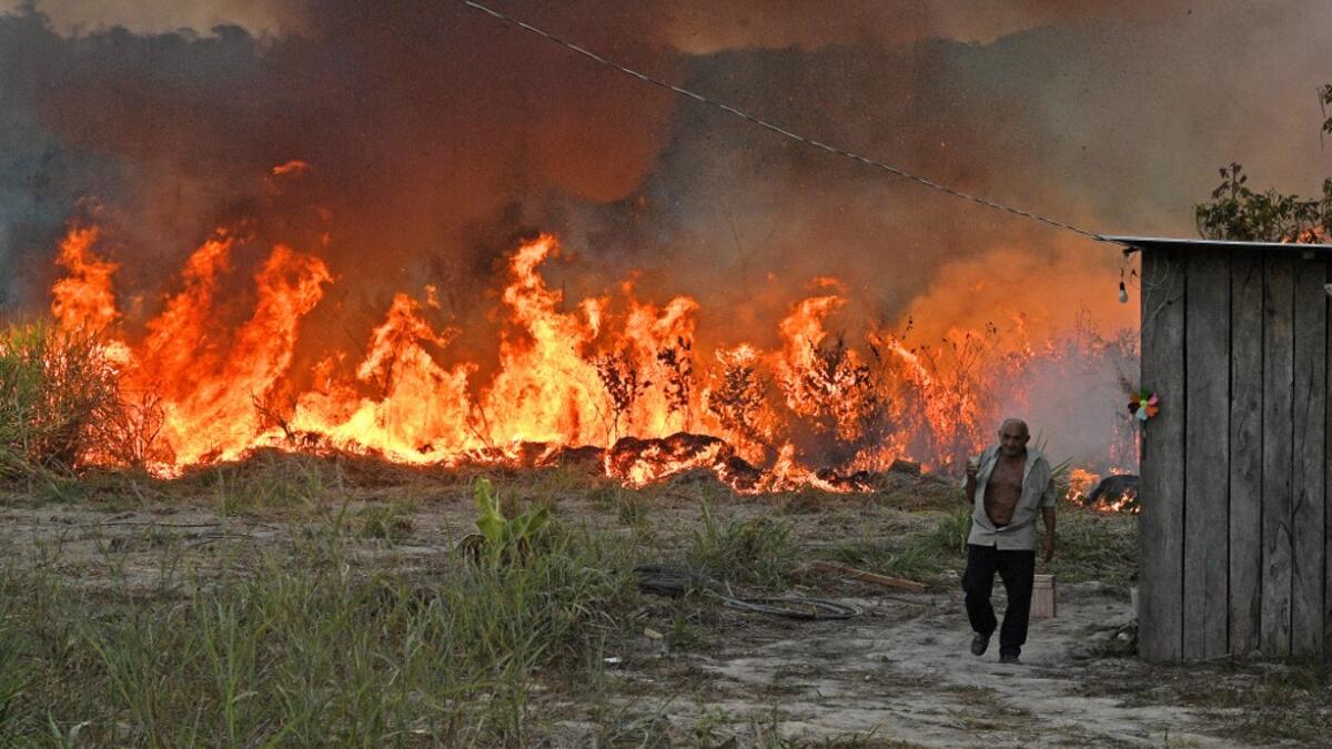 An elderly farmer who set fire to rainforest around his property walks away as the fire approaches their house in an area of Amazon rainforest, south of Novo Progresso in Para state, Brazil, on August 15, 2020. CARL DE SOUZA / AFP