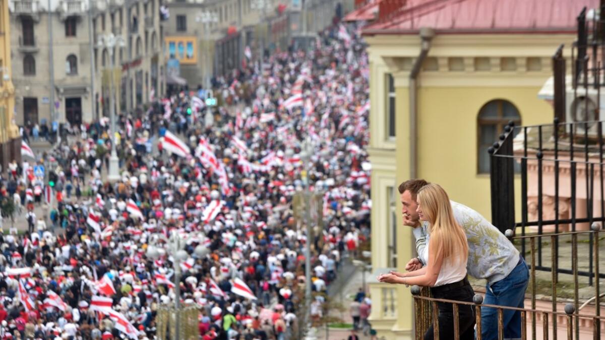 A couple looks at demonstrators from a balcony during a march of opposition supporters to protest against disputed presidential elections results in Minsk on August 23, 2020. Sergei GAPON / AFP