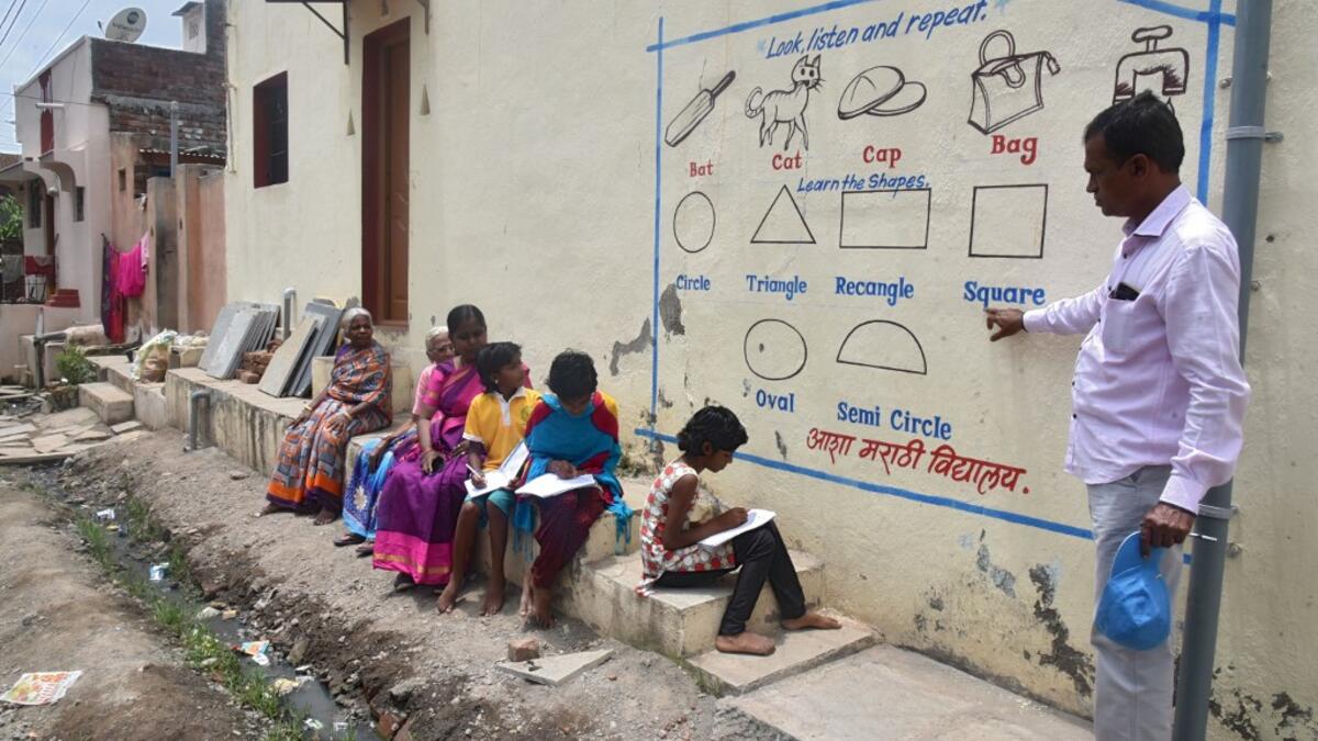 In this picture taken on August 27, 2020, Kalidas Chavdekar, a school teacher of Aasha Marathi Vidyalay points to a writing from textbooks of various subjects painted on the wall of a house to teach students who are unable to carry smartphones to attend online school classes amid Covid-19 coronavirus pandemic in Solapur, in Maharashtra state. AFP