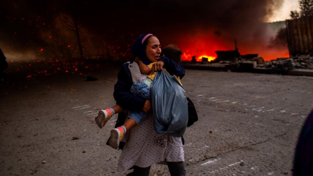 A migrant holds a girl as they flee a fire burning in the Moria camp on the island of Lesbos on September 9, 2020. Thousands of asylum seekers on the Greek island of Lesbos fled for their lives on September 9, 2020 as a huge fire ripped through the camp of Moria, the country's largest and most notorious migrant facility.