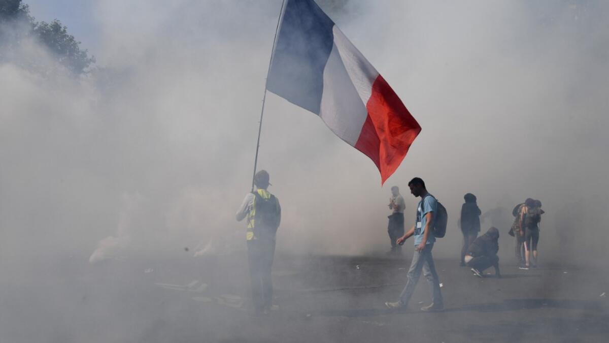 A protester holds a French national flag surrounded by smoke of tear gas during a demonstration called by the "yellow vest" (gilets jaunes) movement on September 12, 2020 in Paris. Alain JOCARD / AFP