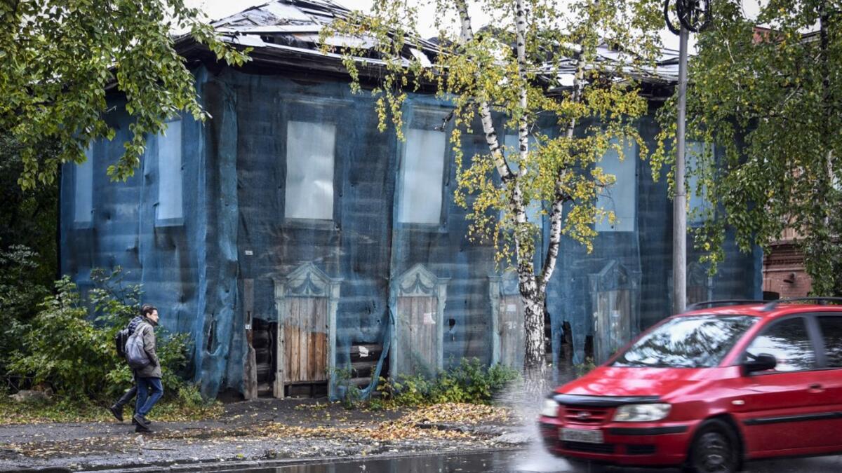 People walk past a traditional wooden house in the Siberian city of Tomsk on September 8, 2020. Tomsk is considered to be one of the oldest towns in Siberia founded in 1604. Wooden architecture is one of the symbols of the city of Tomsk, its distinctive feature. Today Tomsk is the only city in Siberia where the background wooden buildings have been preserved, reflecting the manor structure of the city streets. Unfortunately, many wooden houses are not in very good condition and require restoration. Alexande