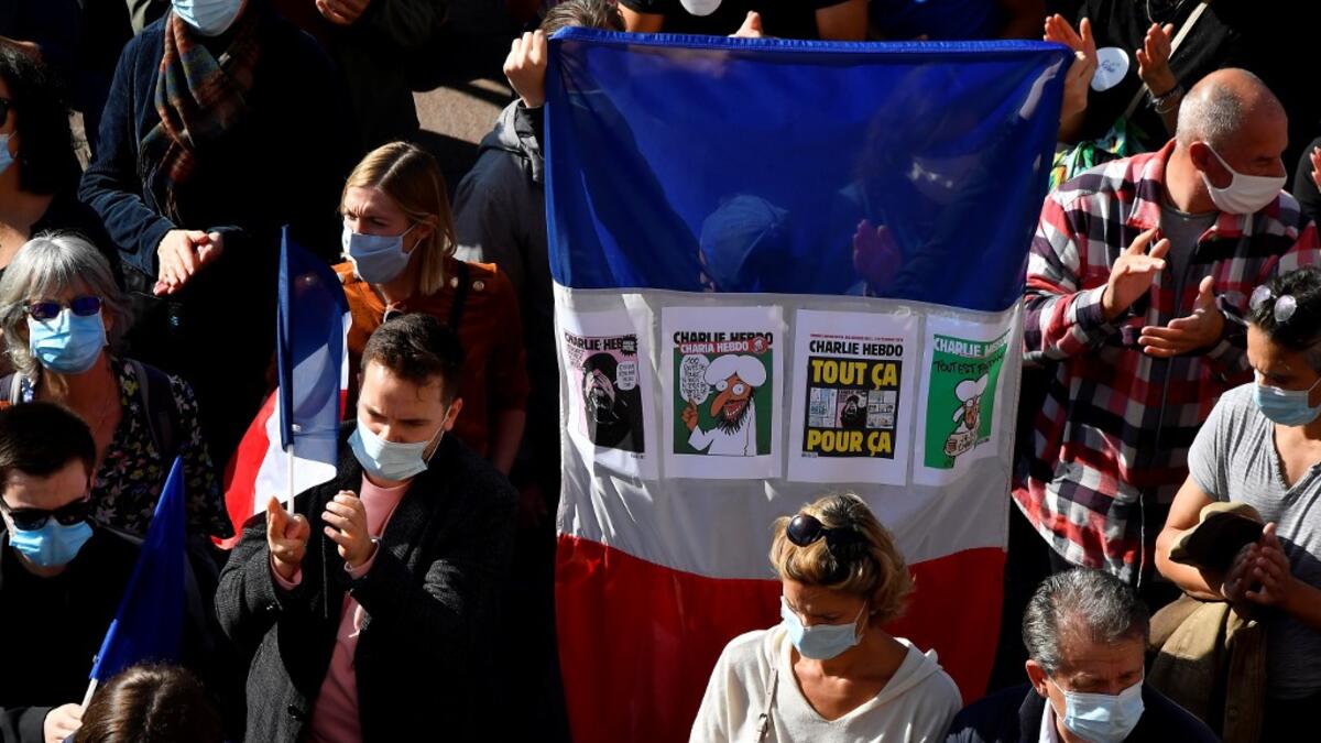 A person holds a French national flag with front covers of Charlie Hebdo satirical magazine as people gather on Place du Capitole in Toulouse on October 18, 2020, in homage to history teacher Samuel Paty two days after he was beheaded by an attacker who was shot dead by policemen. GEORGES GOBET / AFP