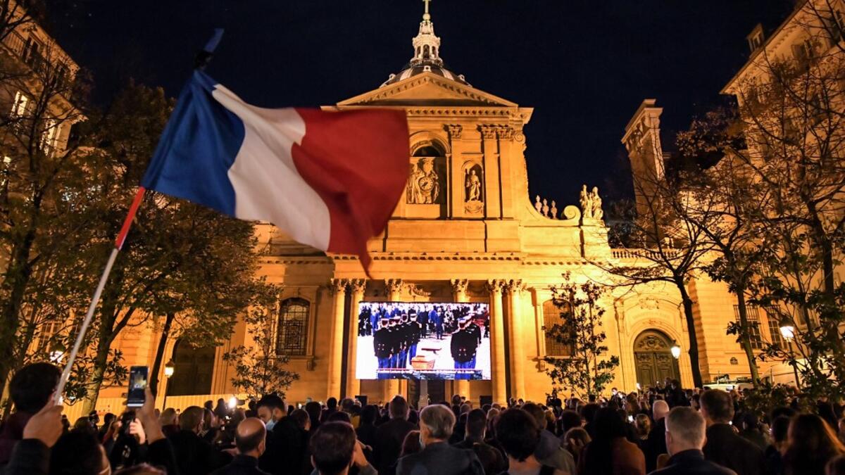 An attendee waves a French flag as people gather on the Place de la Sorbonne in Paris on October 21, 2020, to watch a live broadcast on a giant screen of a national homage at the Sorbonne University to French teacher Samuel Paty, who was beheaded for showing cartoons of the Prophet Mohamed in his civics class. Bertrand GUAY / AFP