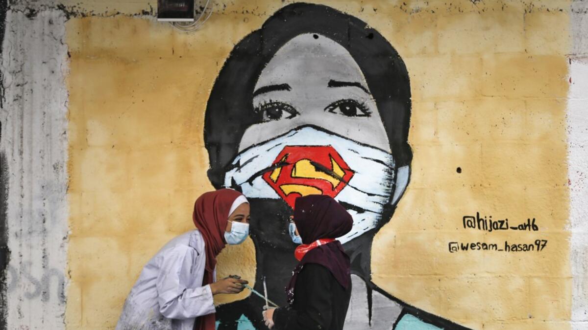 Palestinian students interact as they paint murals of a mask-clad girls in Gaza City on October 22, 2020, amid the novel coronavirus pandemic crises. Mohammed ABED / AFP