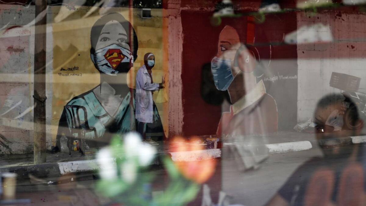 The image of a Palestinian student painting a large mural of a mask-clad girl is reflected on the window of a cafe in Gaza City on October 22, 2020, amid the novel coronavirus pandemic crises. Mohammed ABED / AFP