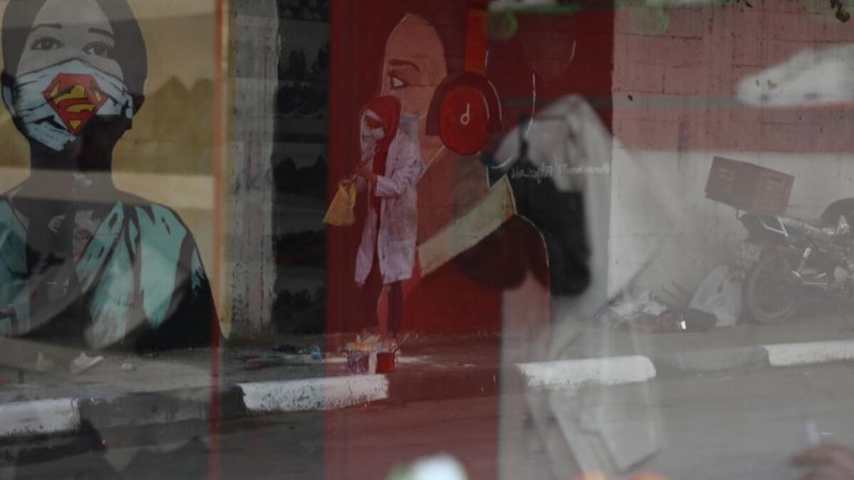 The image of a Palestinian student painting a large mural of a mask-clad girl is reflected on the doors of a shop in Gaza City on October 22, 2020, amid the novel coronavirus pandemic crises. (Instagram)