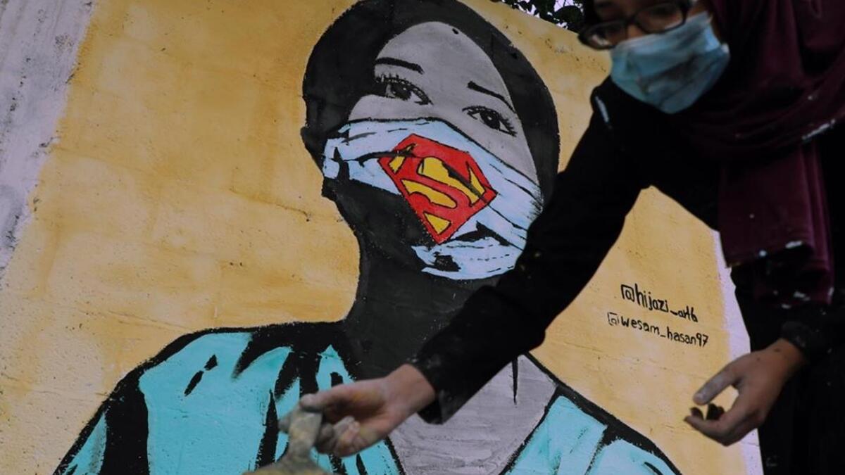 The image of a Palestinian student painting a large mural of a mask-clad girl is reflected on the doors of a shop in Gaza City on October 22, 2020, amid the novel coronavirus pandemic crises. (Instagram)