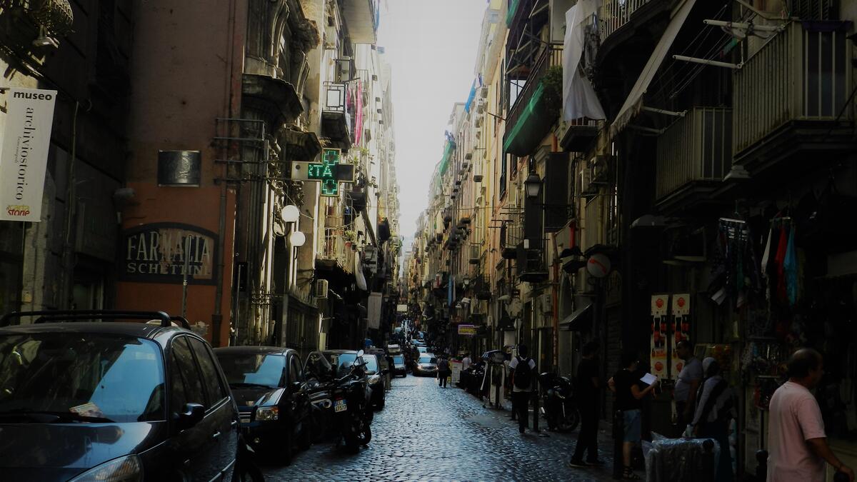 Narrow dark street with cobblestones pavement of historical Naples downtown with typical Mediterranean apartment houses with tiny balconies and wooden/Photo by Ewelina Lepionko