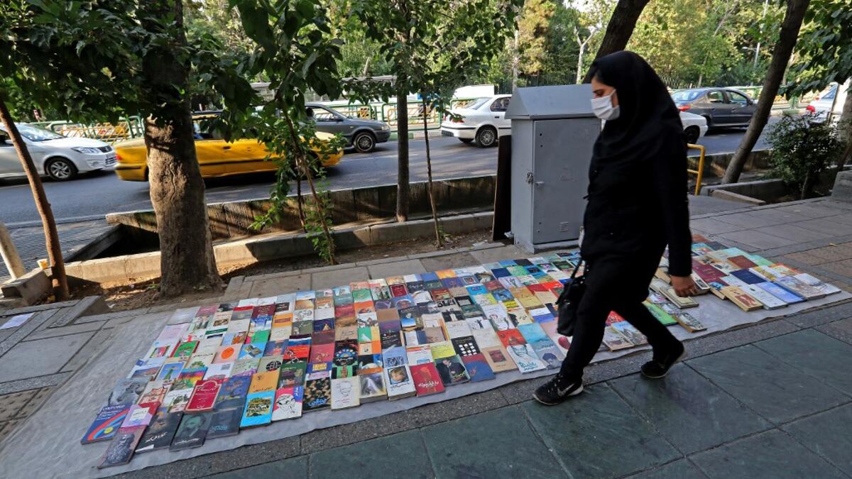 A woman walks past books displayed for sale along a pavement on Enqelab (Revolution) street in Iran's capital Tehran, on September 8, 2020. ATTA KENARE / AFP