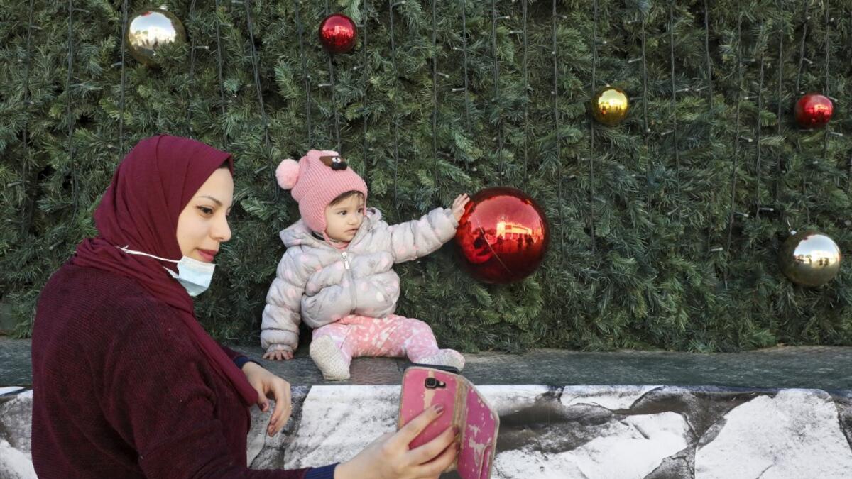 A Palestinian mother takes a picture of her daughter under a Christmas tree near the Church of the Nativity, in the West Bank city of Bethlehem on December 21, 2020. HAZEM BADER / AFP