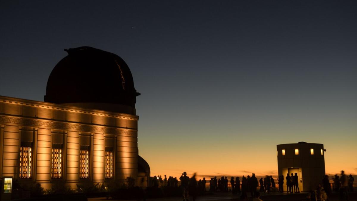 People watch the planets Jupiter and Saturn, upper left, above a telescope dome, during the great conjunction as seen from the Griffith Observatory on the same day as the winter solstice, December 21, 2020 in Los Angeles, California. The great conjunction refers to the astronomical alignment of Jupiter and Saturn, the closest for nearly 400 years. Patrick T. Fallon / AFP