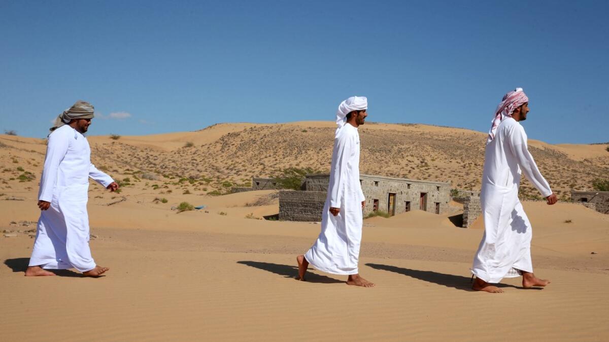 Former inhabitants of Wadi al-Murr, walk near abandoned houses in the Omani village, about 400 kms (250 miles) southwest of the capital Muscat, on December 31, 2020. Encroaching desert sands have left little evidence that Wadi al-Murr ever existed, but former inhabitants, while resigned to its destruction, are trying to preserve its memory. MOHAMMED MAHJOUB / AFP