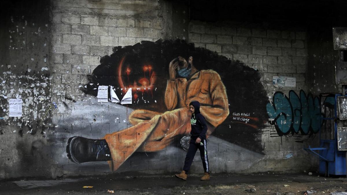 A young boy walks past a mural painting with writing in Arabic that reads "we are tired" near Al-Nour square in the northern city of Tripoli, following overnight clashes between security forces and anti-government protesters, on January 29, 2021. More than 400 people have been wounded in northern Lebanon this week in clashes between security forces and protesters angered by a coronavirus lockdown they say is starving them. JOSEPH EID / AFP