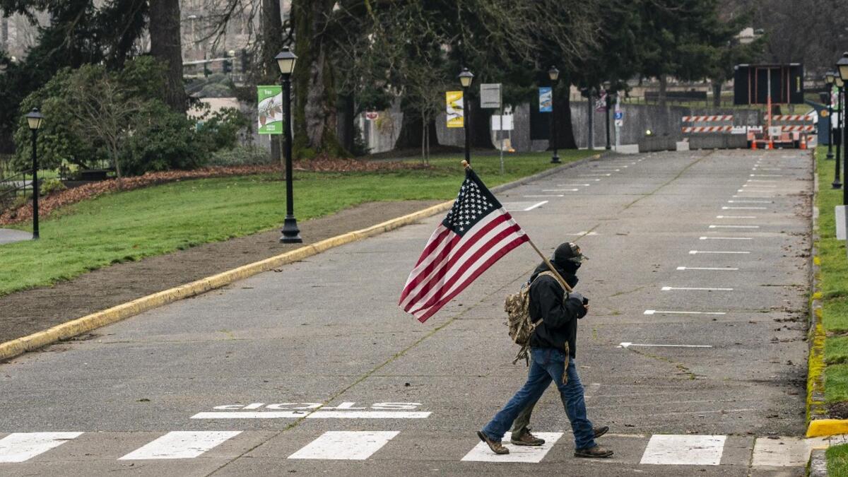 A man walks with a U.S. flag on the Washington State Capitol campus on January 20, 2021 in Olympia, United States. One Donald Trump protester held a sign at an otherwise quiet capitol campus on Presidential Inauguration Day today. David Ryder/Getty Images/AFP