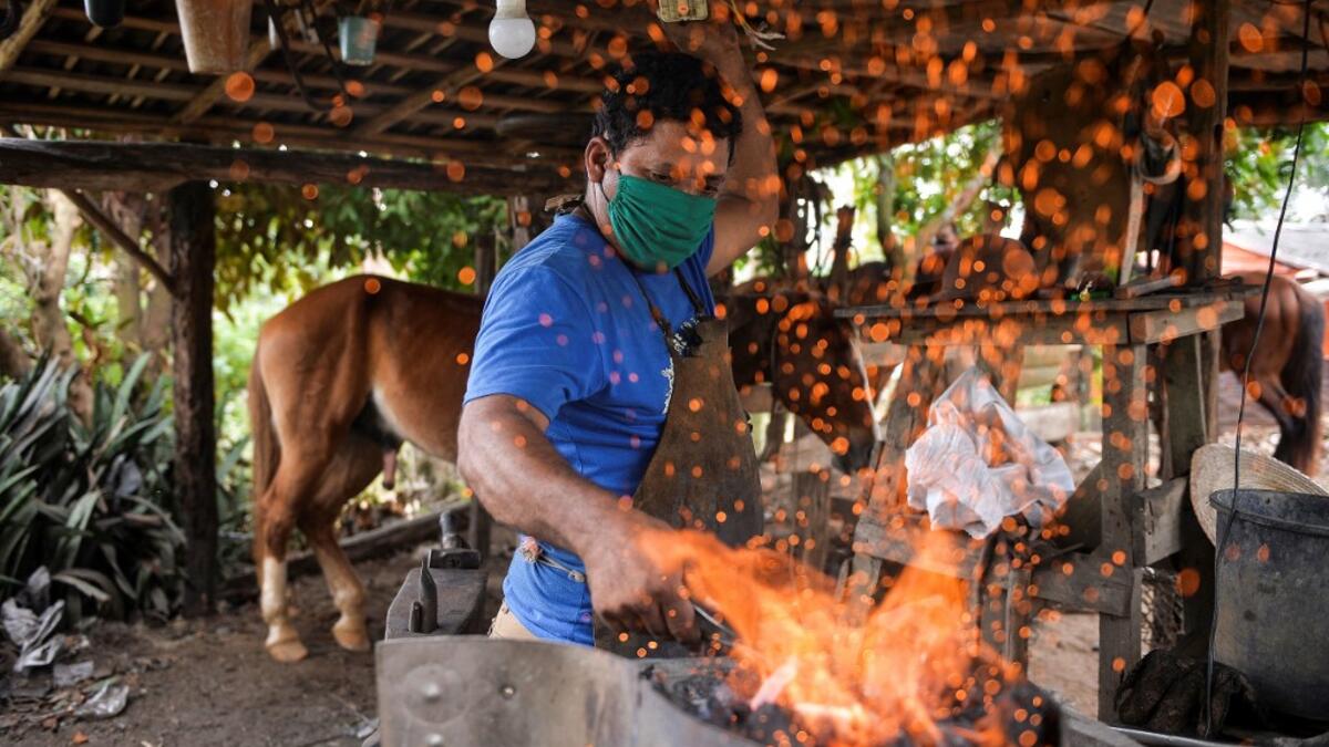 Yusmani Garcia, a blacksmith and tour guide, makes a horseshoe at his house in Vinales, Cuba, on January 28, 2021. At the foot of the majestic rock formations of Vinales, the terraces of the restaurants look empty and the lodgings have closed. With the arrival of COVID-19, the incipient prosperity of this Cuban town came to a halt and people abandoned tourism jobs to return to work the land. YAMIL LAGE / AFP