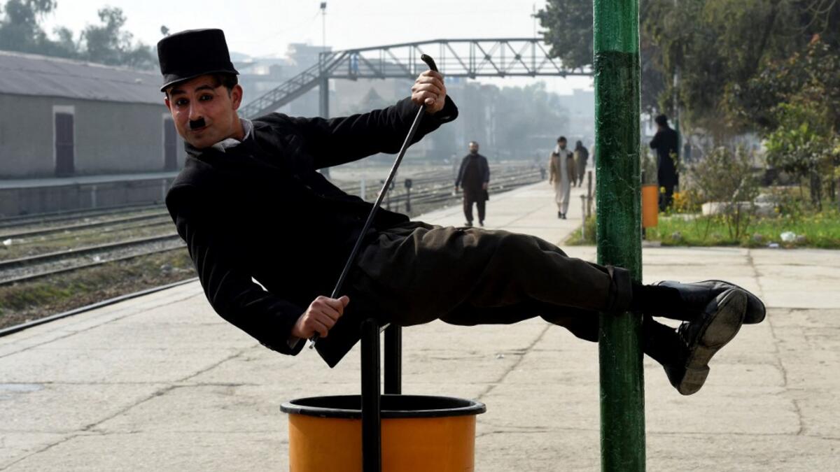In this picture taken on February 9, 2021, street actor Usman Khan, dressed up as silent film star Charlie Chaplin, performs at a train station in the Pakistan's northwestern city of Peshawar. Wearing a bowler hat and familiar toothbrush moustache, Pakistan's Usman Khan darts through traffic swinging a cane, teasing motorists and shopkeepers for laughs and a few rupees with a Charlie Chaplin impersonation that has become a viral sensation.  Abdul MAJEED / AFP