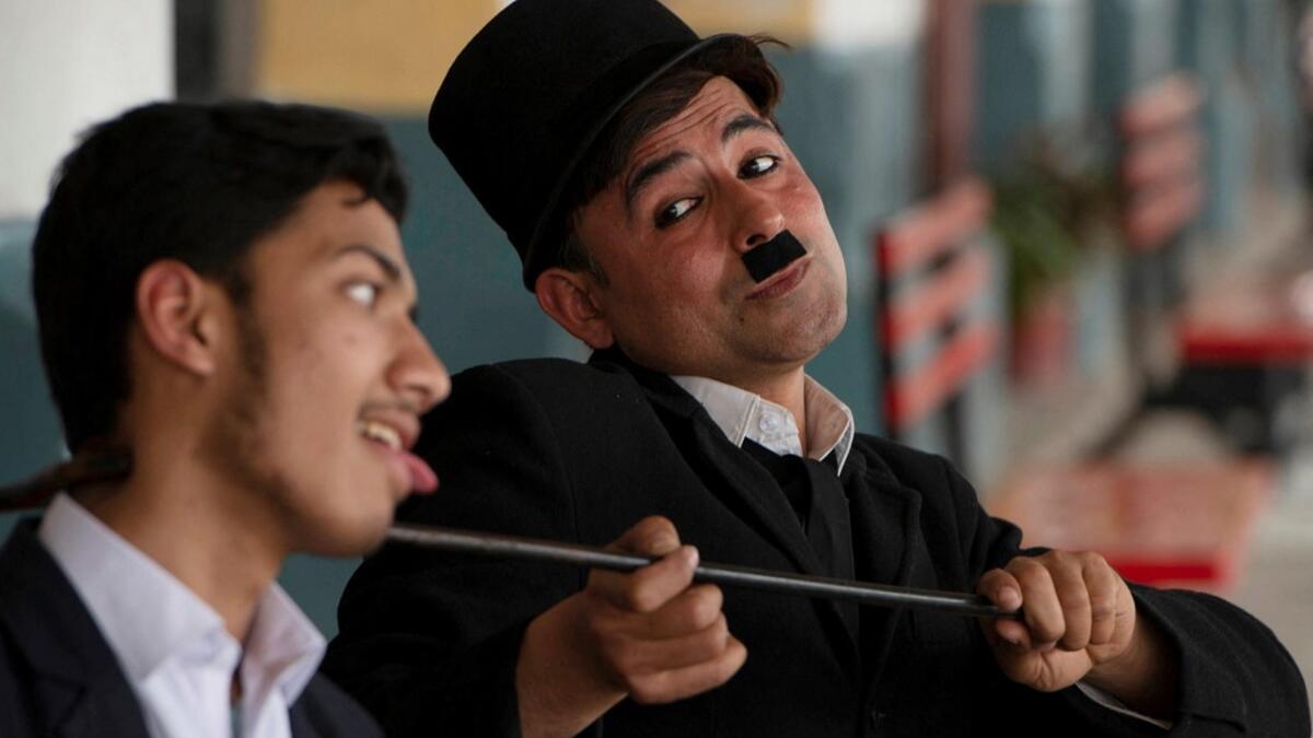 In this picture taken on February 9, 2021, street actor Usman Khan (R), dressed up as silent film star Charlie Chaplin, performs in the Pakistan's northwestern city of Peshawar. Wearing a bowler hat and familiar toothbrush moustache, Pakistan's Usman Khan darts through traffic swinging a cane, teasing motorists and shopkeepers for laughs and a few rupees with a Charlie Chaplin impersonation that has become a viral sensation.  Abdul MAJEED / AFP