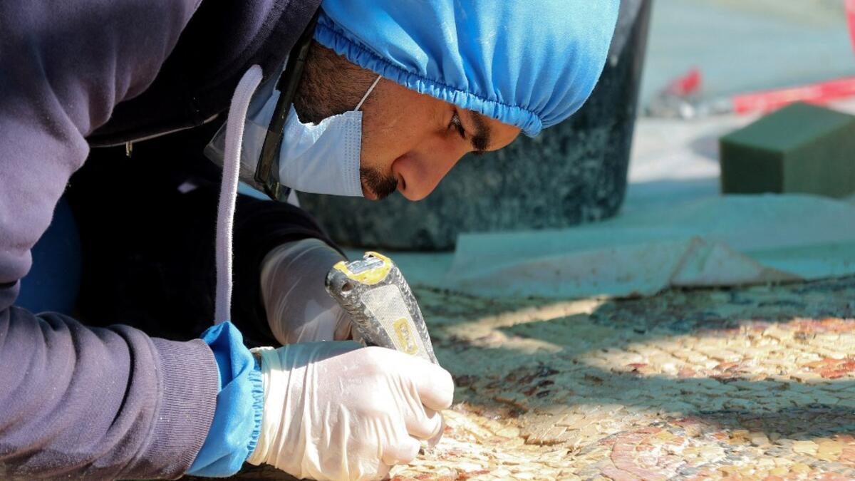 A worker employed by a pilot project run by the UN cultural agency UNESCO, restores a mosaic floor at an ancient church complex, in the small town of Rihab, some 70 kilometres north of the Jordanian capital Amman, on February 9, 2021. In the ruins of the ancient Byzantine church in Jordan, local townspeople and Syrian refugees work side by side on a project that unites preserving cultural heritage and fighting poverty.  Khalil MAZRAAWI / afp