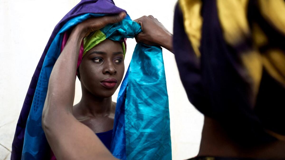 A dresser helps a gold miner to wear a turban in the backstage prior to take part in a fashion show as part of the first edition of the International Gold Fair Afrik'Or, in Bamako, on February 12, 2021. The Princess of Burundi Esther Kamatari, selected 34 women among gold mines workers in southern Mali, to walk down the catwalk for a fashion show organised during the International Gold Fair. Gold represents 15% of Mali's exports and more than 20% of its GDP estimated at nearly US$20 billion by the end of 20