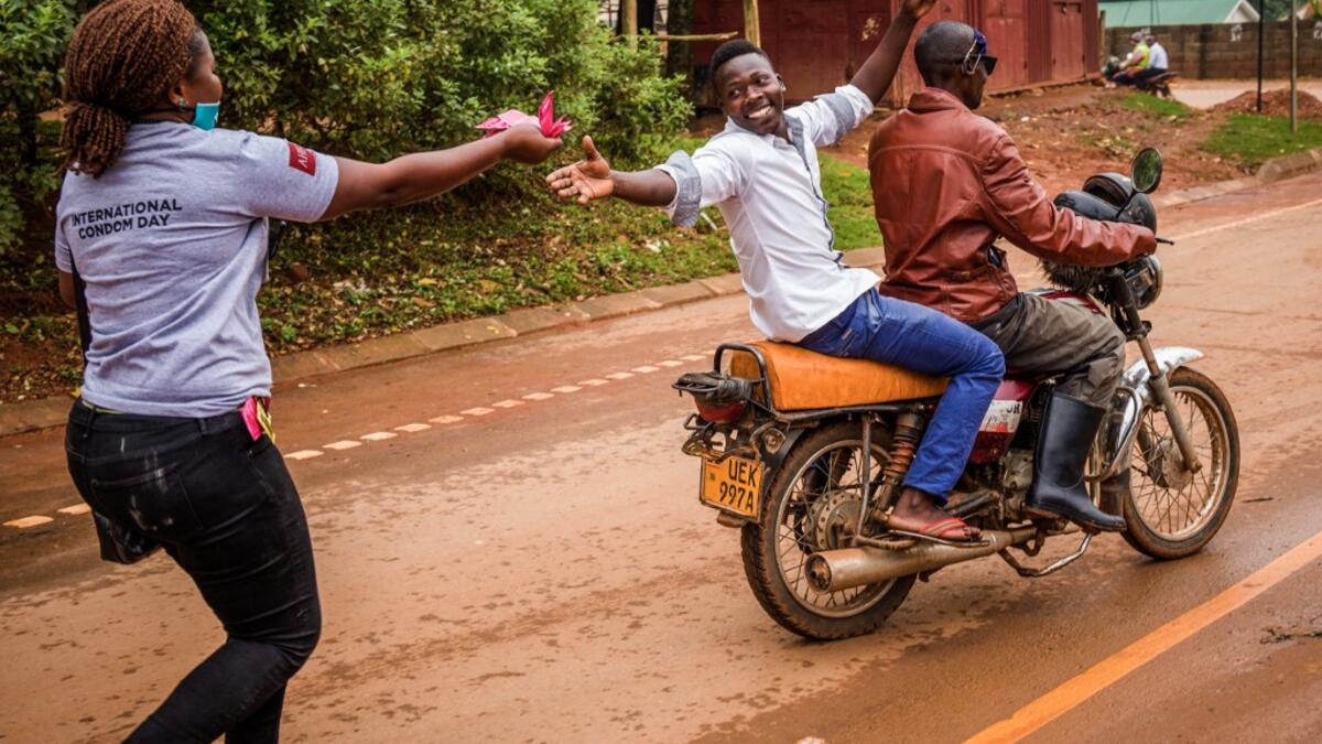 A man sitting on a motorbike catches condoms from a health worker delivering free condoms on the international condom day, in the streets of Kampala on February 13, 2021, ahead of Valentine’s day. Badru KATUMBA / AFP