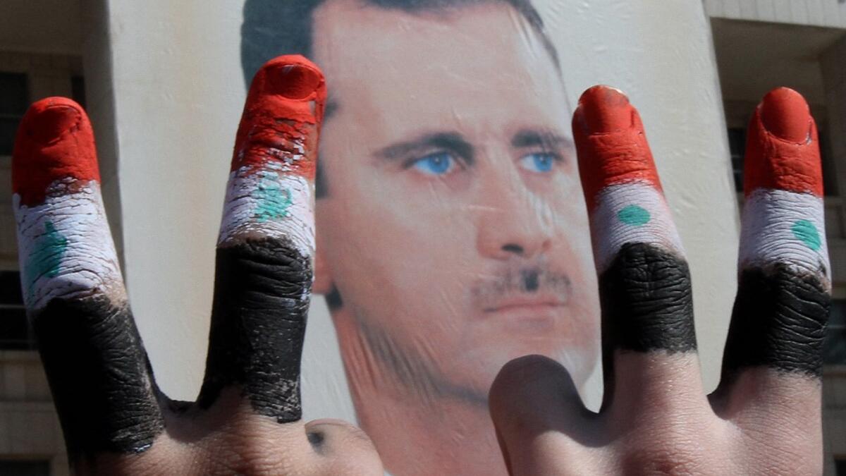 Two men, with the fingers painted in the colours of the Syrian flag, show the V-sign as they pose in front of a huge image of President Bashar al-Assad