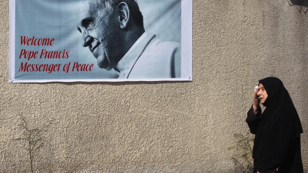 An Iraqi woman walks in front of a banner welcoming Pope Francis
