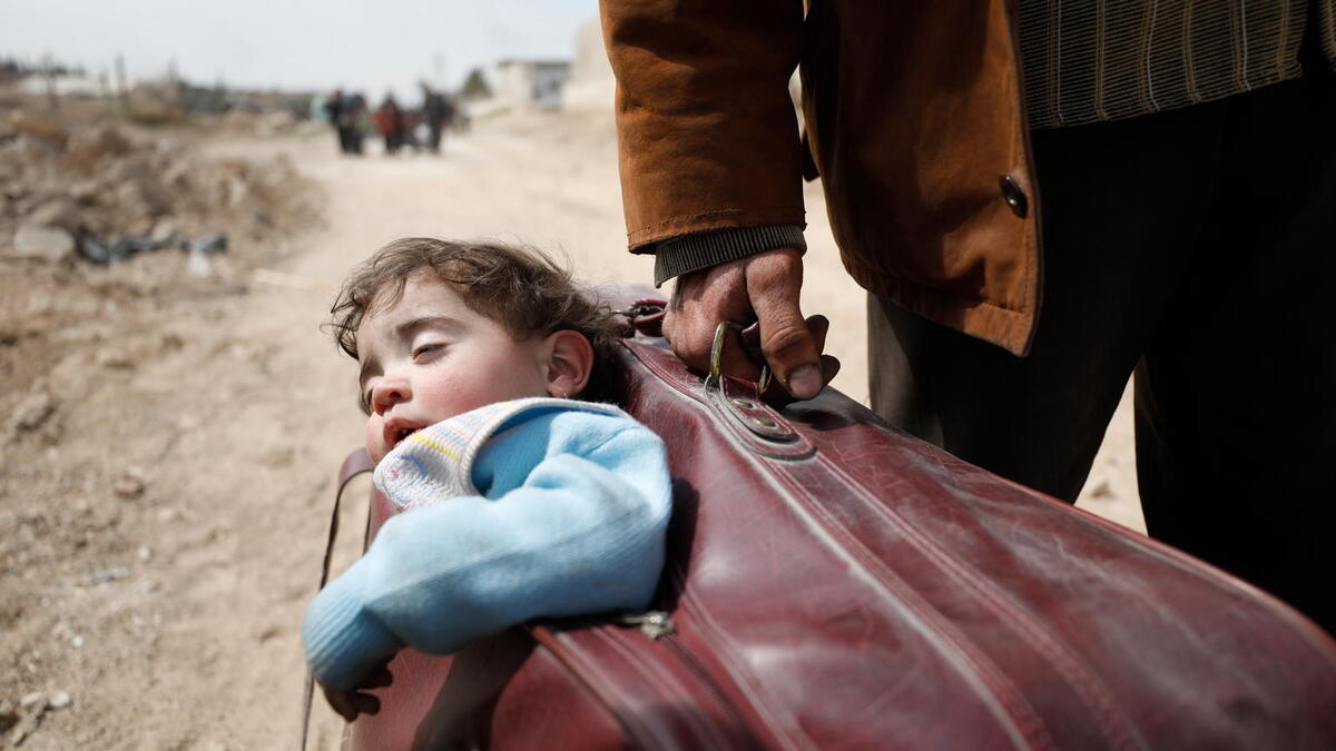 On 15 March 2018 in Beit Sawa, eastern Ghouta, a man carrying a child in a suitcase walks towards Hamourieh where an evacuation exit from eastern Ghouta has been opened.