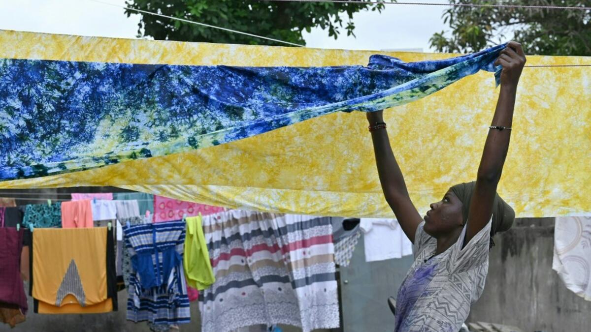 A woman hangs up dyed cotton fabric to dry at Pathe'O house in the popular district of Treichville in Abidjan on March 31, 2021. A small self-taught tailor in his early years, the Ivorian-Burkinabe Pathe'O became the designer of African heads of state and celebrates the fiftieth anniversary of his brand, leading the "fight" for the recognition of fashion on the continent